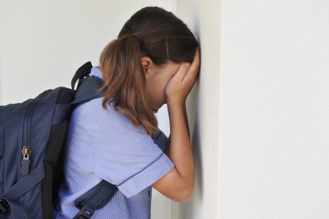Sad young schoolgirl covering her face and crying against a wall